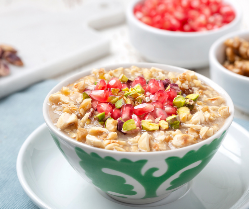Bowl of oatmeal with pomegranate and pistachios on a light blue surface