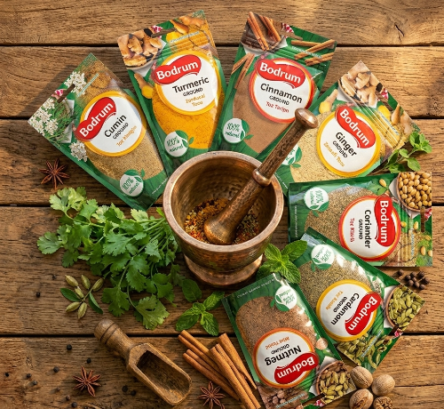 Bodrum brand spice packages on a wooden surface with herbs and spices.